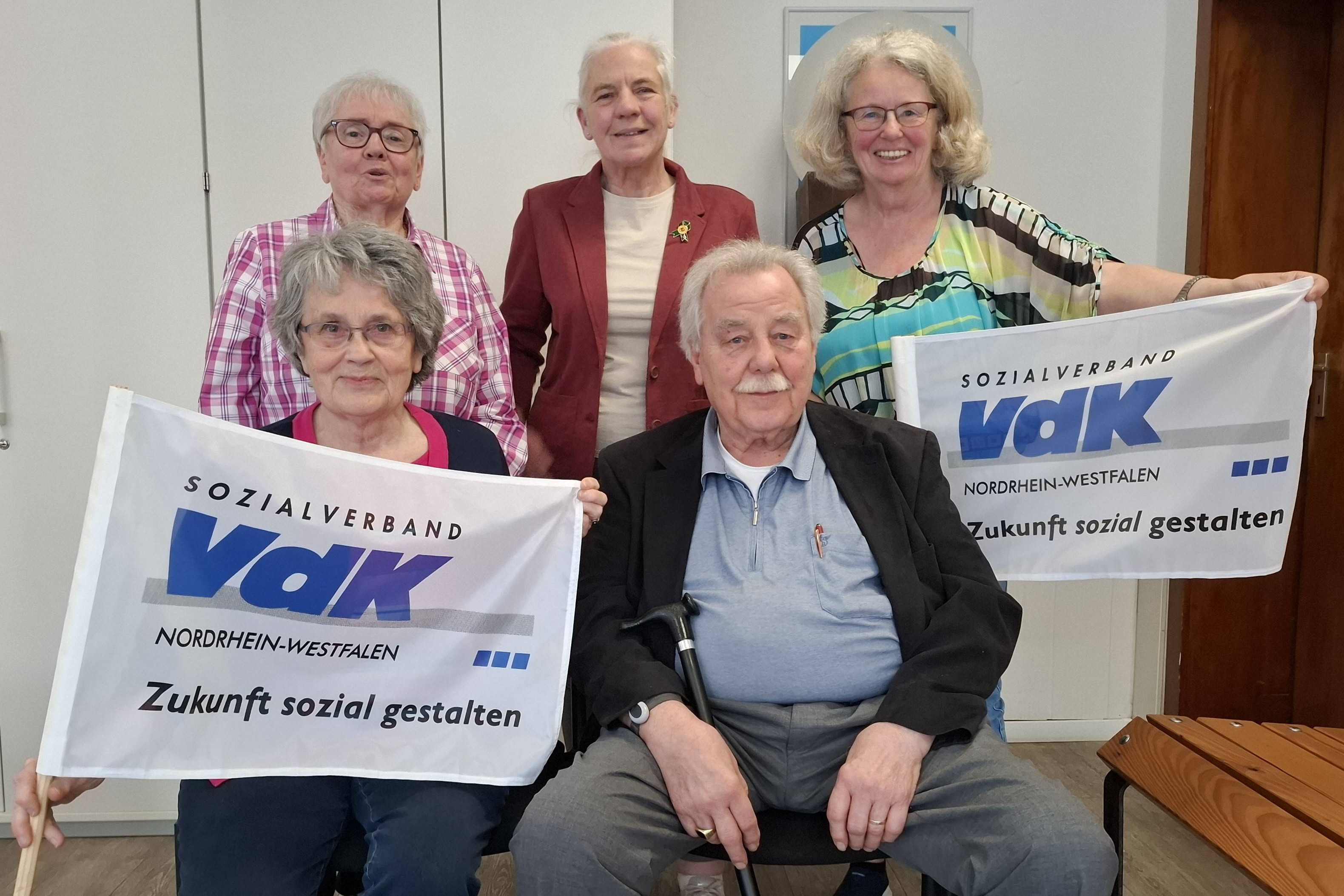 Der neue VdK Vorstand im Kreis Mülheim an der Ruhr Zu sehen ist der neue VdK Vorstand im Kreisverband Mülheim an der Ruhr. Der neue Kassierer Ernst Osterhage fehlt aus gesundheitlichen Gründen. Die Personen halten 2 VdK Fahnen hoch.