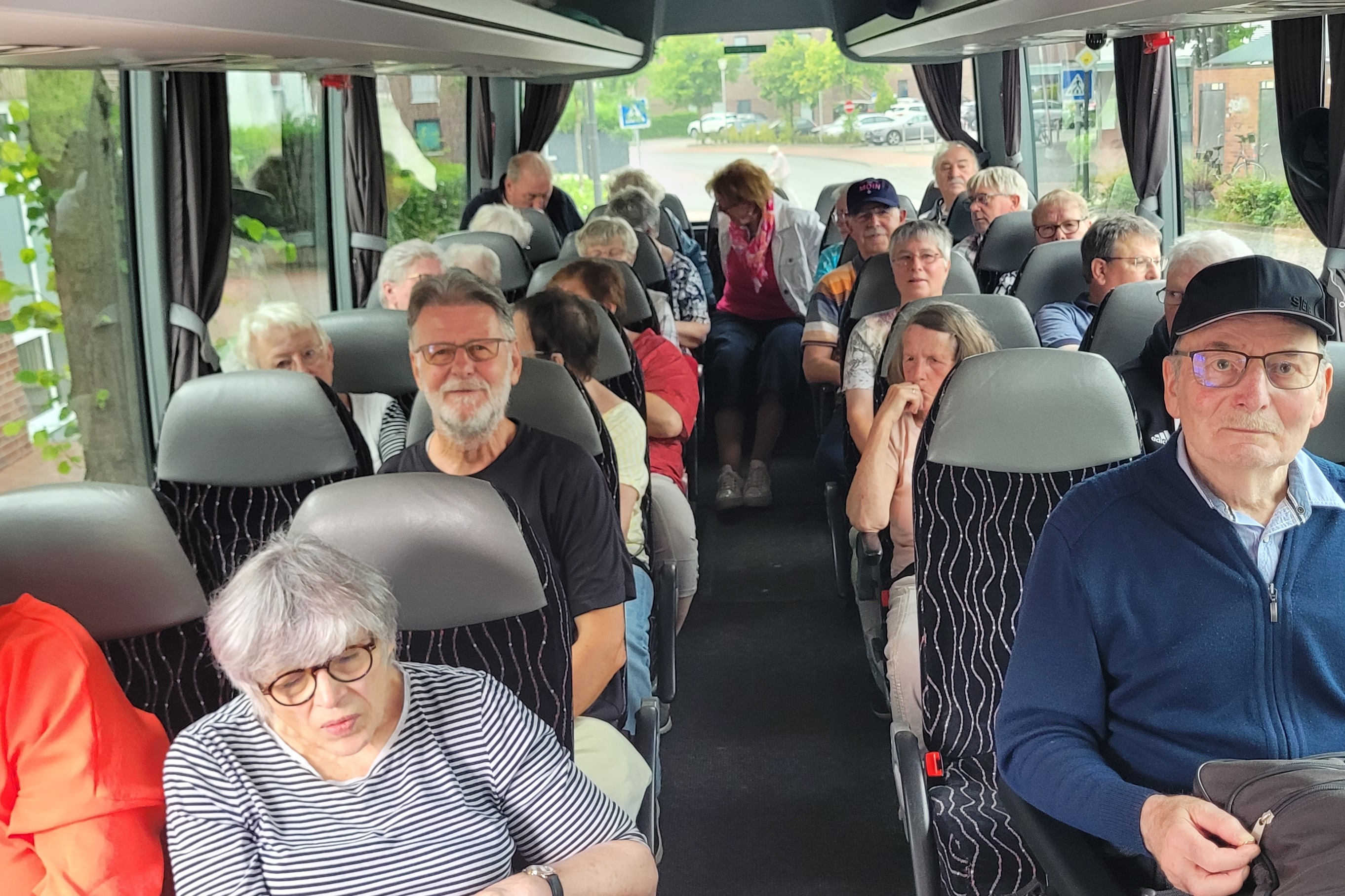Die Mitglieder sitzen im Bus. Vorne rechts ein Rollstuhlfahrer in seinem Rollstuhl, gesichert im Bus..