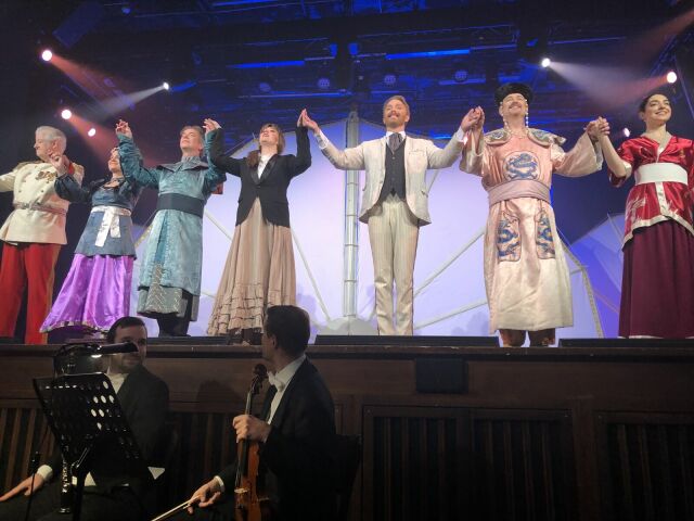 Bunt kostümierte Schauspieler der Operette "Land des Lächelns" stehen auf der Bühne, um Applaus entgegenzunehmen.