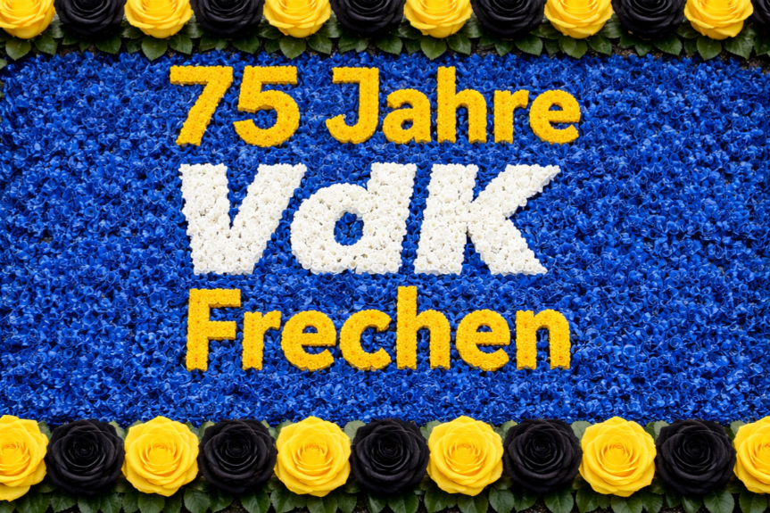 In der Art eines Maiherzens ist der Text "75 Jahre VdK Frechen" aus gelben und wei&szlig;en Bl&uuml;ten in eine Umgebung aus blauen Bl&uuml;ten gesteckt worden