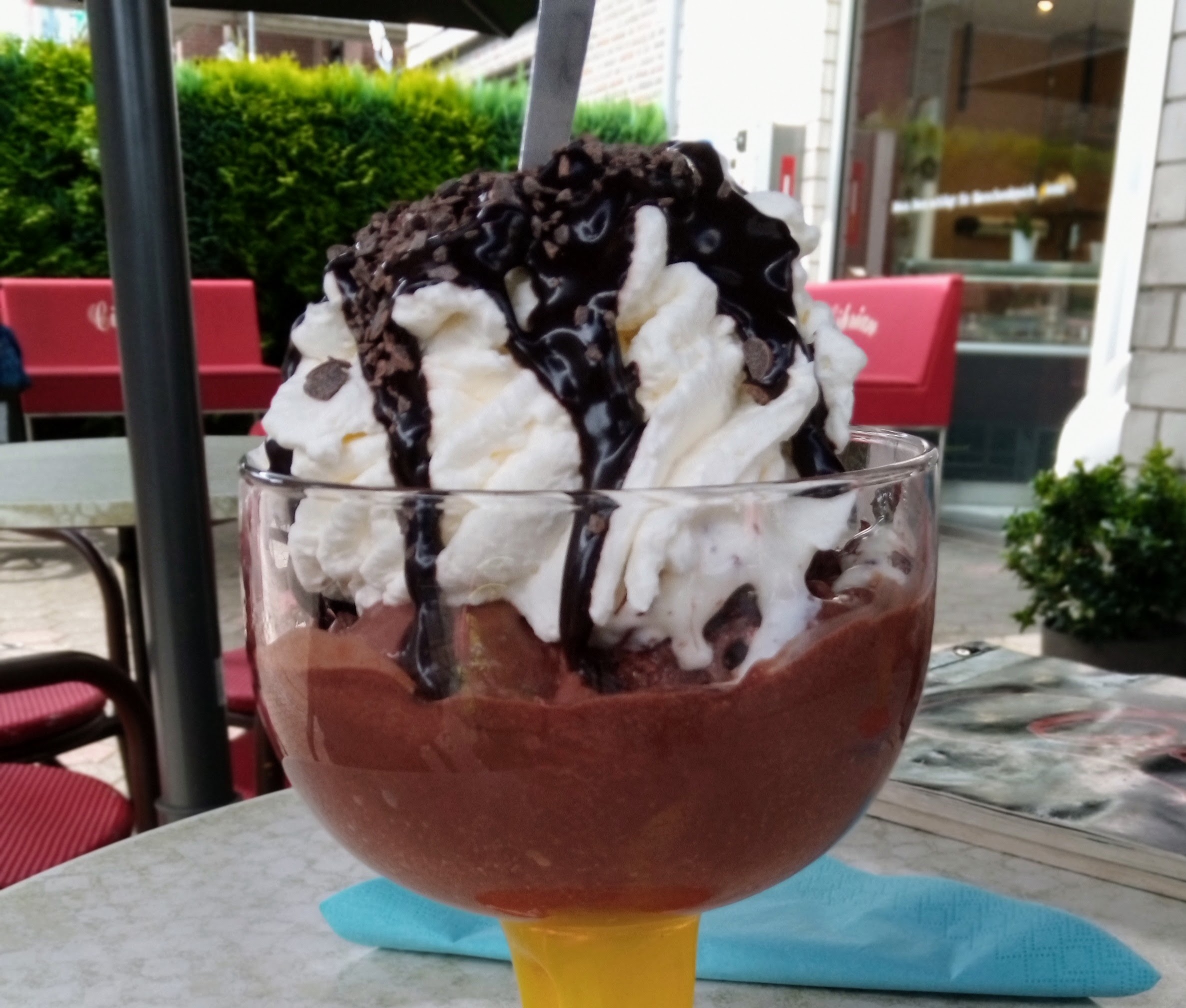 Ein großer Eisbecher aus Glas mit Schokoladeneis, Sahne und Schokosauce steht auf einem Tisch garniert mit einem Schild, auf dem reserviert steht.