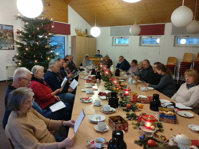 Viele Menschen sitzen an einem weihnachtlich gedeckten Tisch