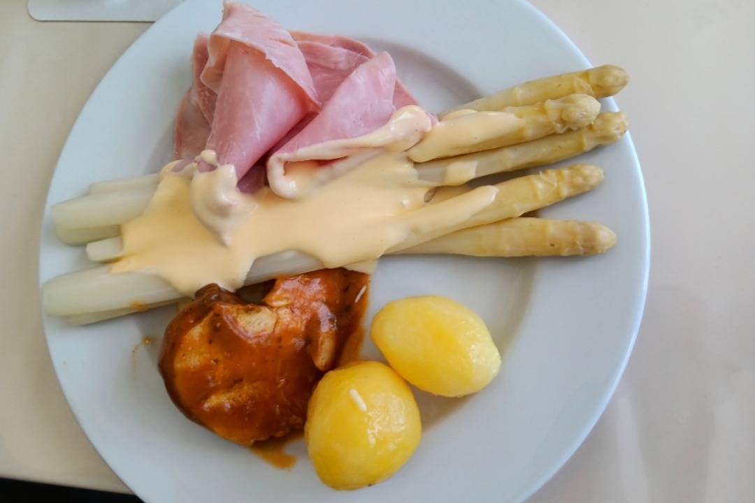 Man sieht einen Porzellanteller mit Spargelstangen, Kartoffeln, So&szlig;e und ein Schweinemedaillon
