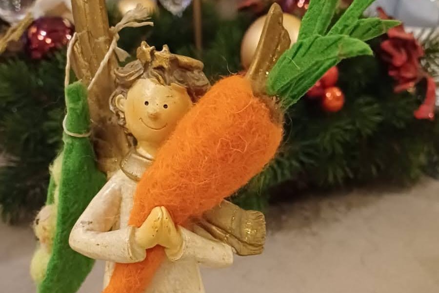 Ein Stoffengel h&auml;lt in den H&auml;nden eine M&ouml;hre aus Filz und tr&auml;gt auf einer Schulter Erbsen aus Filz.