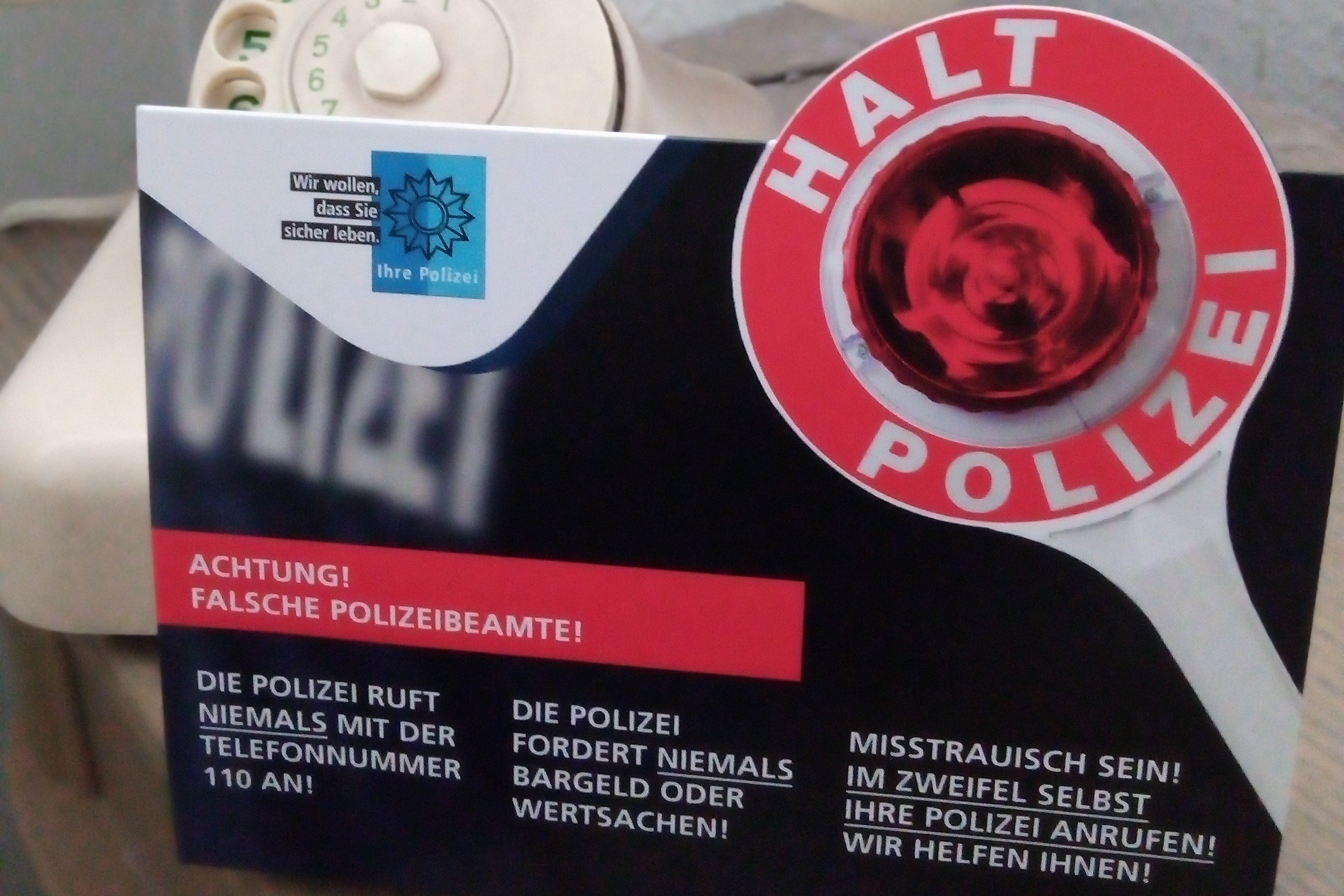 Das Bild zeigt einen Aufsteller der Polizei mit Hinweisen vor einem Telefon.