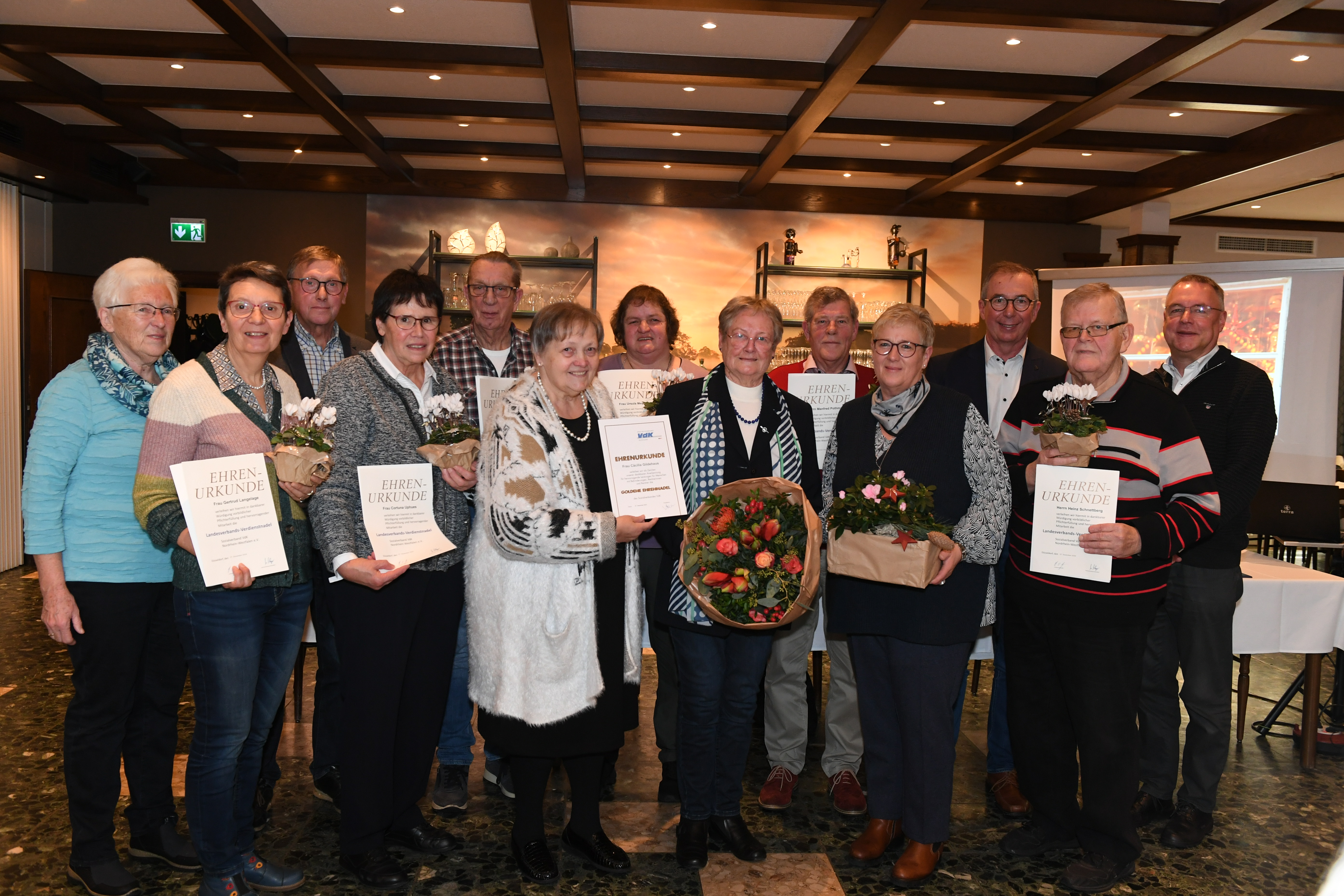 VdK-Kreis-Vorstandsmitglied Eveline Gerdes (6.v.l.) hält die Urkunde für Cäcilia Gildehaus (6.v.r.), die die Goldene Verdienstnadel für 26 Jahre Vorstandsarbeit erhielt. 500. Mitglied ist Christa Maaßmann (4.v.r.). | Foto: Heinrich Weßling