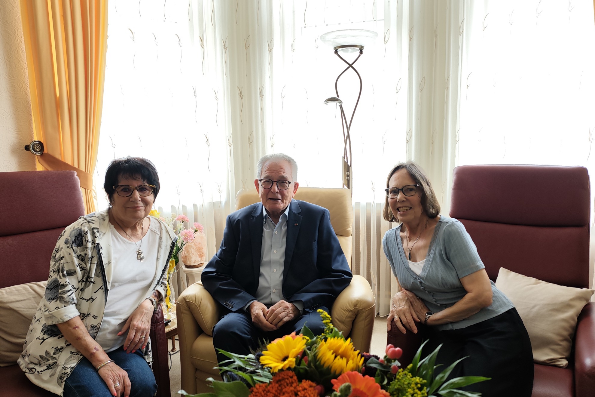Zwei Frauen und zwischen ihnen sitzt ein Mann der seinen 90. Geburtstag feiert.