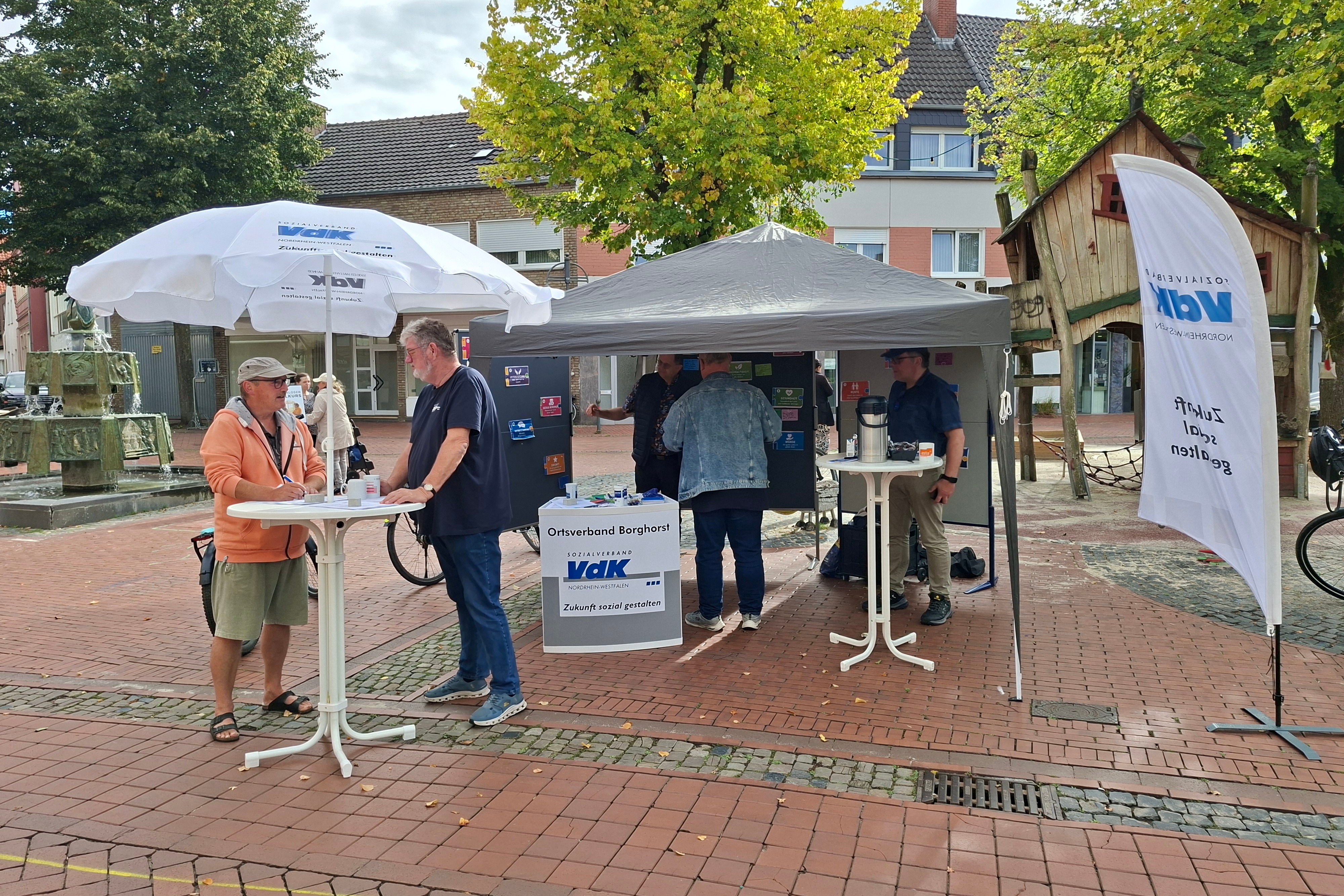 Marktstand in Borghorst Marktstand in Borghorst, mit Sonnenschirm und Zeltpavillon. Am Stehtisch steht Herr Meiers und unterhält sich mit einem Gast.