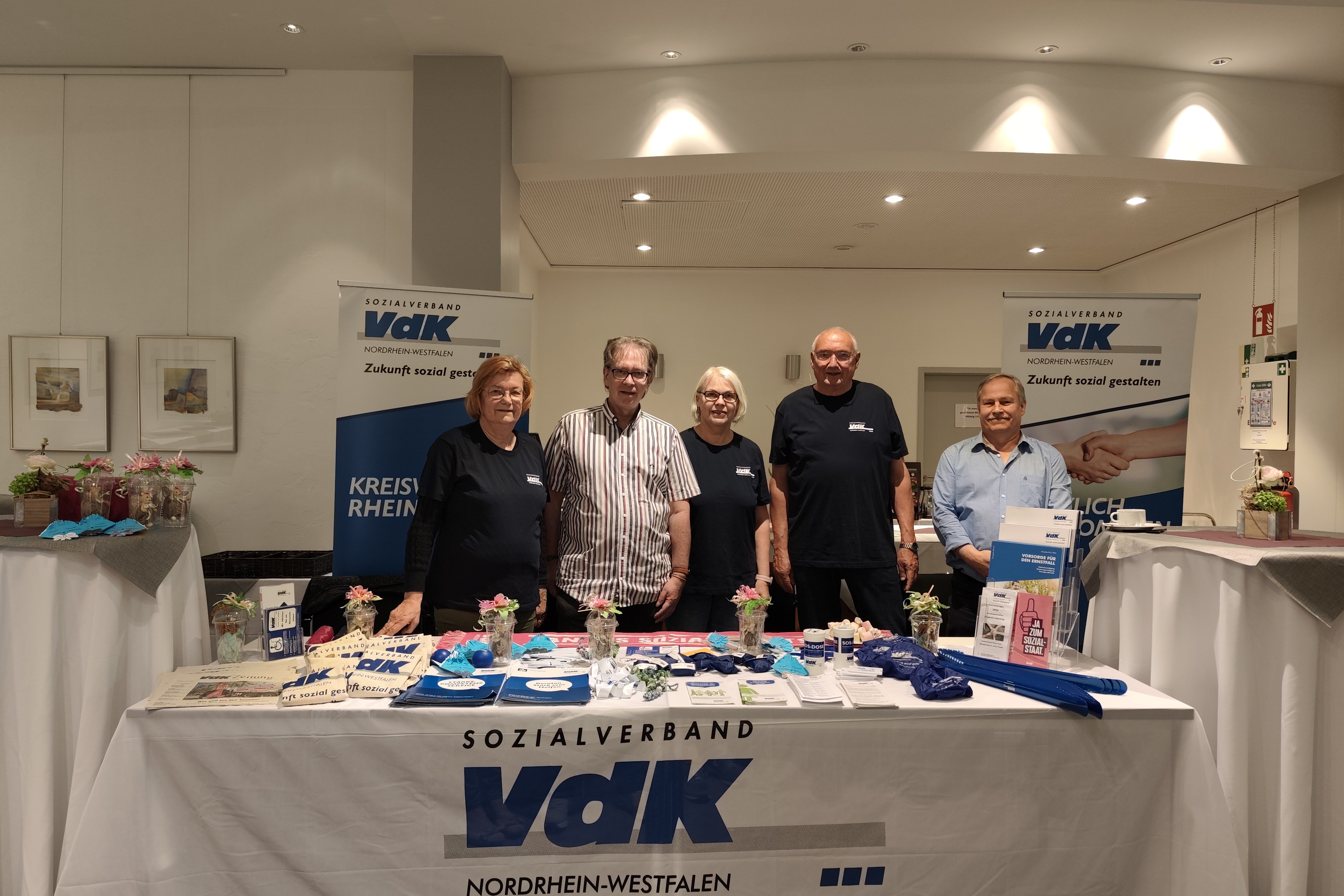 Von links nach rechts: Wilma Kirschmer, Michael Stawicki, Martina Buttgereit, Bernd vom Felde und Jürgen Dittmann (VdK OV Essen-Ruhrhalbinsel) am Informationsstand. 5 Personen stehen hinter dem VdK Informationsstand.
