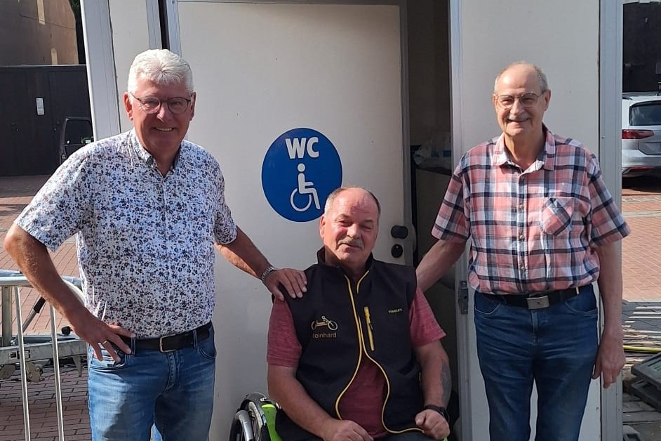 Toilette Ortsverbandsvorsitzender Karl-Heinz Hermsen (links) und Rolf Grootens, Mitglied im Vorstand (rechts) freuen sich, dass mit Hilfe der SPD Uedem und Firmeninhaber Ralf Jansen aus Uedem für Rollstuhlfahrer wie Reinhard Domke eine Zwischenlösung gefunden wurde und während des Streetfood-Festivals eine mobile, behindertengerechte Toilette aufgestellt werden konnte.